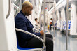 Side view of African American male entrepreneur in suit sitting in modern underground carriage and messaging on cellphone while commuting to work