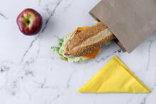 Top View Of Tasty Nutritious Sandwich In Takeaway Paper Bag Placed On Marble Table With Fresh Red Apple
