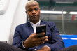 © David Munoz/ADDICTIVE STOCK - From below African American male entrepreneur in suit sitting in modern underground carriage and messaging on cellphone while commuting to work