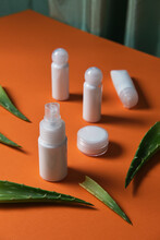 Top View Of Facial Skin Care Products In White Plastic Jars And Leaves Of Aloe Vera Plant Placed On Orange Background In Studio