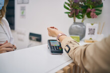 Unrecognizable female client making payment on POS terminal with smart watch in beauty center
