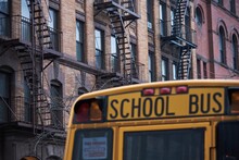 Traditional Yellow School Bus Driving Along Street In New York City On Cloudy Day