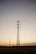 © Gustavo Pozo/ADDICTIVE STOCK - Low angle of tall electricity towers and wires in field under evening sky with sun setting over horizon line in summertime