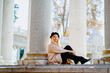 © Jake Jakab/ADDICTIVE STOCK - Side view of smiling female wearing coat and beret sitting near stone column in autumn park looking at camera