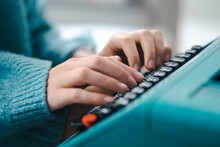 Crop view of anonymous female author sitting on sofa and using vintage typewriter while creating interesting story