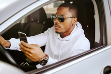Side View Of Rich Determined African American Male Driver Sitting In Parked Car And Browsing Smartphone