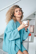 © Jake Jakab/ADDICTIVE STOCK - Side view of smiling female in oversize warm sweater sitting on staircase with a cup of coffee in apartment and looking at camera