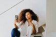 © Jake Jakab/ADDICTIVE STOCK - Young ethnic curly haired female in casual white blouse and jeans taking self portrait on mobile phone while sitting on stairway at home