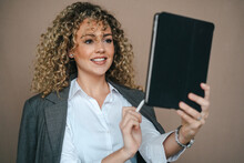 Cheerful Female Entrepreneur In Formal Outfit Using Tablet With Stylus And Rejoicing Over Project Accomplishment On Brown Background In Studio