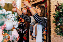 Side View Of Mature Female Friends Buying Christmas Ornaments Inside Decor Shop Looking At Baubles On Christmas Tree
