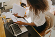 © Jake Jakab/ADDICTIVE STOCK - High angle side view of female bookkeeper sitting at table in home office and analyzing financial reports and paper documents during remote work