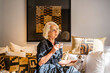 © Javier De La Torre/ADDICTIVE STOCK - Peaceful pensive mature female in elegant dress drinking coffee and stroking dog while relaxing on cozy soft sofa with cushions in stylish living room