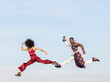 © Jose Carlos Cerdeno/ADDICTIVE STOCK - Side view of African American couple in trendy traditional clothes jumping high above asphalt road and performing dance on background of blue sky