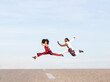 © Jose Carlos Cerdeno/ADDICTIVE STOCK - Side view of African American couple in trendy traditional clothes jumping high above asphalt road and performing dance on background of blue sky