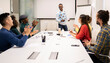 © Jose Carlos Cerdeno/ADDICTIVE STOCK - Cheerful multiracial coworkers sitting around table and applauding to male speaker during presentation and discussion of business strategy in modern workplace
