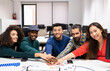 © Jose Carlos Cerdeno/ADDICTIVE STOCK - Young multiracial successful startup team gathering around table with diagrams and stacking hands together while discussing business strategy in modern office