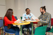 © Jose Carlos Cerdeno/ADDICTIVE STOCK - Cheerful young creative multiracial coworkers in casual outfits gathering around tables with papers and sharing ideas about new project during meeting in modern workspace