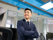 © Jose Carlos Cerdeno/ADDICTIVE STOCK - Cheerful young Asian male manager in formal suit looking away while standing near table with computers in contemporary coworking office