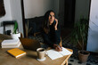 © Joy Zamora/ADDICTIVE STOCK - Busy ethnic female entrepreneur sitting at table in home office and speaking on cellphone about new startup project while working remotely and looking away
