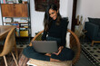 © Joy Zamora/ADDICTIVE STOCK - Cheerful Indian female sitting in wicker chair and having video call on laptop while smiling