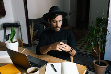 From above male entrepreneur browsing mobile app and working with diagrams at home