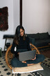 © Joy Zamora/ADDICTIVE STOCK - Indian female freelancer sitting with crossed legs in wicker chair and typing on netbook while working online from home