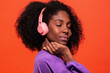 © Manuel Ruiz/ADDICTIVE STOCK - Modern unemotional black woman with Afro hairstyle wearing pink headphones and listening to music on red background