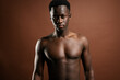 © Luis Manuel Munoz/ADDICTIVE STOCK - Confident African American young male with muscular naked torso standing in trendy jeans with hand on waist on brown background in studio and looking at camera