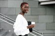 © Luis Manuel Munoz/ADDICTIVE STOCK - Side view of positive elegant young black business lady with cup of takeaway coffee standing near modern urban building