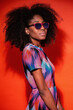 © Manuel Ruiz/ADDICTIVE STOCK - Modern Cuban woman with Afro hair wearing bright dress and sunglasses in red studio background