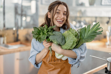 Portrait of pretty smiling woman with fresh broccoli, roman salad, basil on the kitchen with steam on background. Healthy green vegetable concept. Close up. High quality photo