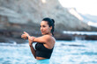 © Pablo Garcia/ADDICTIVE STOCK - Concentrated fit female in sports bra standing in seashore and warming up while stretching arms before training and looking away