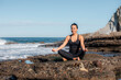 © Pablo Garcia/ADDICTIVE STOCK - Smiling female in activewear sitting with crossed legs on rocky beach and doing yoga in Lotus pose with mudra hands