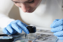 Woman In Rubber Gloves Looking At Dollar Bills Through Magnifying Glass