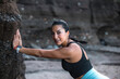 © Pablo Garcia/ADDICTIVE STOCK - Side view of cheerful female with fit body leaning on rock on seashore and stretching body while warming up before workout and looking at camera
