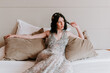 © Mauricio Garay/ADDICTIVE STOCK - Calm female in sparkling elegant dress resting on comfortable bed with pillows while touching hair and looking away
