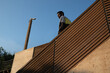 © Oscar De Dios/ADDICTIVE STOCK - From below of young pensive African American guy in casual outfit listening to music in wireless earphones standing on staircase of modern building against cloudless blue sky