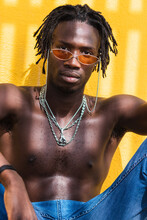 Serious Young African American Guy With Naked Torso And Dreadlocks Wearing Trendy Sunglasses And Metal Chains And Looking At Camera