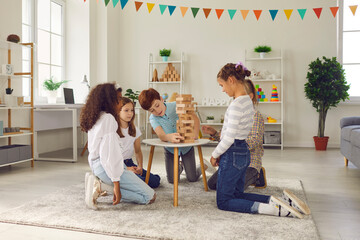 Children playing with educational toys in cozy after-school centre. Group of quiet diverse 8-10-year-old kids busy with interesting wood block tower stacking board game during birthday party at home