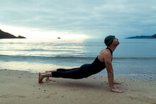 Side View Of Professional Male Swimmer In Swimsuit And Cap Stretching Body On Sandy Seashore Before Training
