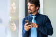© Joao - Businessman looking through window with the cell phone on his hand. Happy successful male portrait at the office by the window