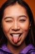 © Victor Torres/ADDICTIVE STOCK - Close-up portrait of happy Asian young woman. She wears a purple jacket and is looking at camera smiling and winking against a yellow background