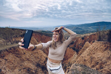 Cheerful Young Female Tourist Taking Selfie On Smartphone While Standing Among Rocky Sandstone Formations In Highlands