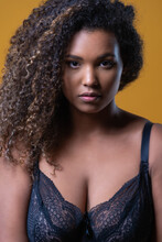 Attractive African American Overweight Female Model With Long Curly Hair Wearing Delicate Lace Bra Looking At Camera Against Yellow Background