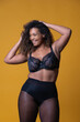 © SERGIO NIEVAS/ADDICTIVE STOCK - Plus size cheerful African American female model with long curly hair wearing elegant lace underwear looking at camera against yellow background