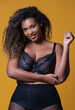 © SERGIO NIEVAS/ADDICTIVE STOCK - Plus size cheerful African American female model with long curly hair wearing elegant lace underwear looking at camera against yellow background