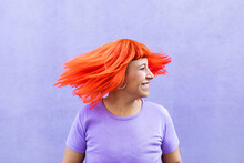 Excited Adult Female With Closed Eyes Shaking Bright Ginger Dyed Hair Against Violet Wall On Street