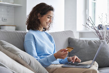Happy Hispanic Young Woman Consumer Holding Credit Card And Laptop Buying Online At Home. Female Shopper Customer Shopping On Ecommerce Website Market Place Making Digital Payment Using Bonus Money.