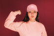 © Victor Torres/ADDICTIVE STOCK - Portrait of funny young asian woman in the studio looking at camera and showing biceps. She is wearing pink clothes over garnet background