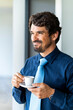 © Joao - Businessman smiling and looking through the window holding a cup of coffee. Happy successful male portrait